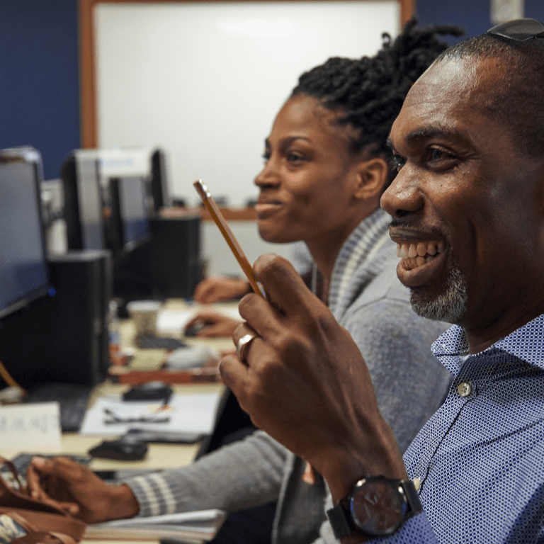Man and woman sitting at row of computers in a classroom.