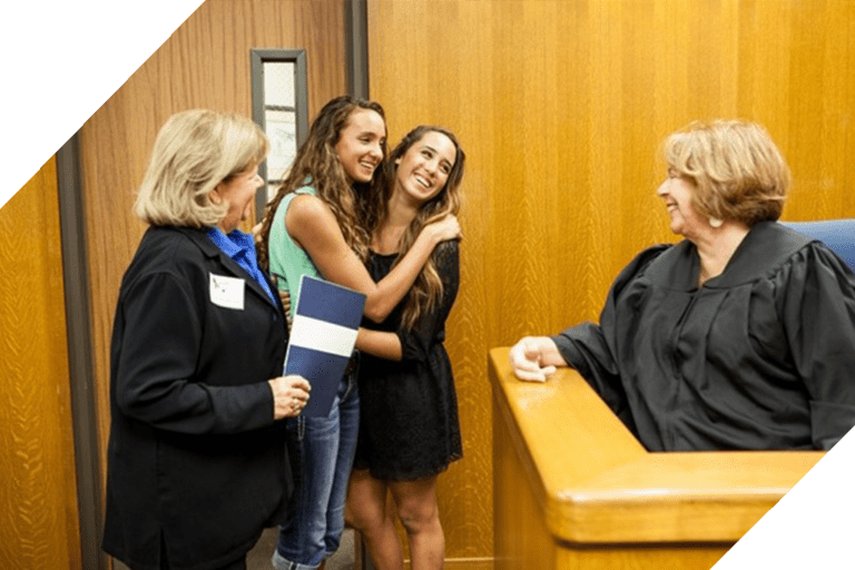 Women smiling with judge and lawyer in courtroom.